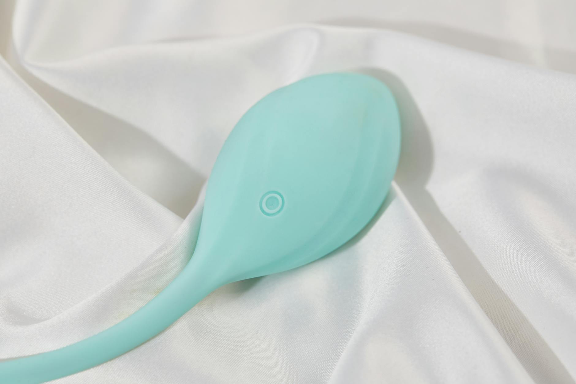 A sleek teal lemon vibrator on white silk fabric, representing modern air-suction pleasure design