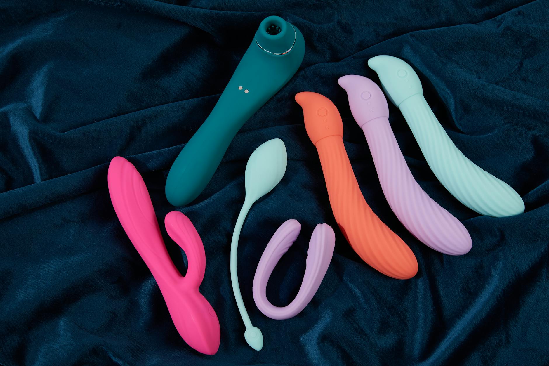 Close-up of a hand holding an orange vibrator against a minimalistic purple backdrop