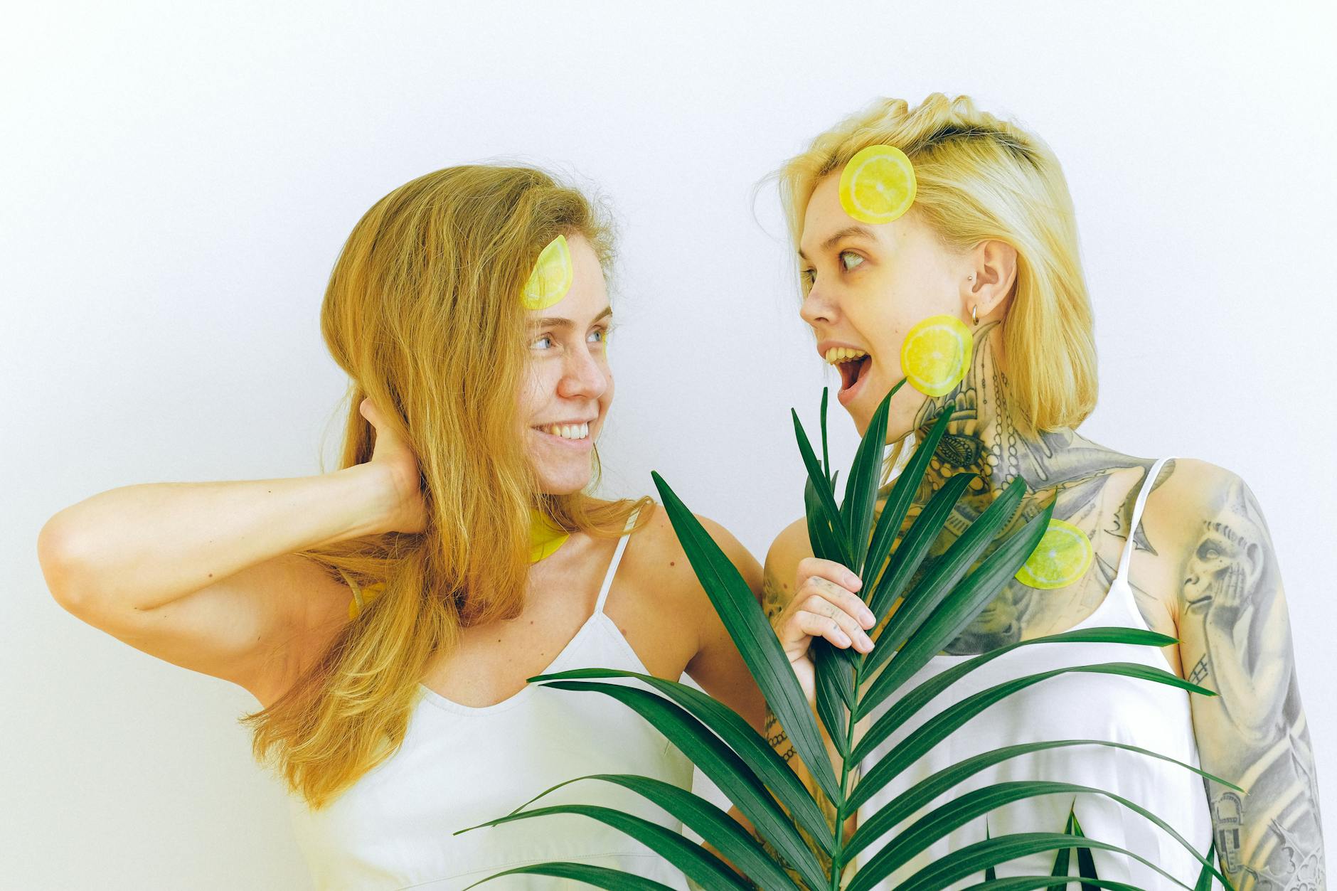 Two women smiling with lemon slices, expressing joy and sensuality indoors