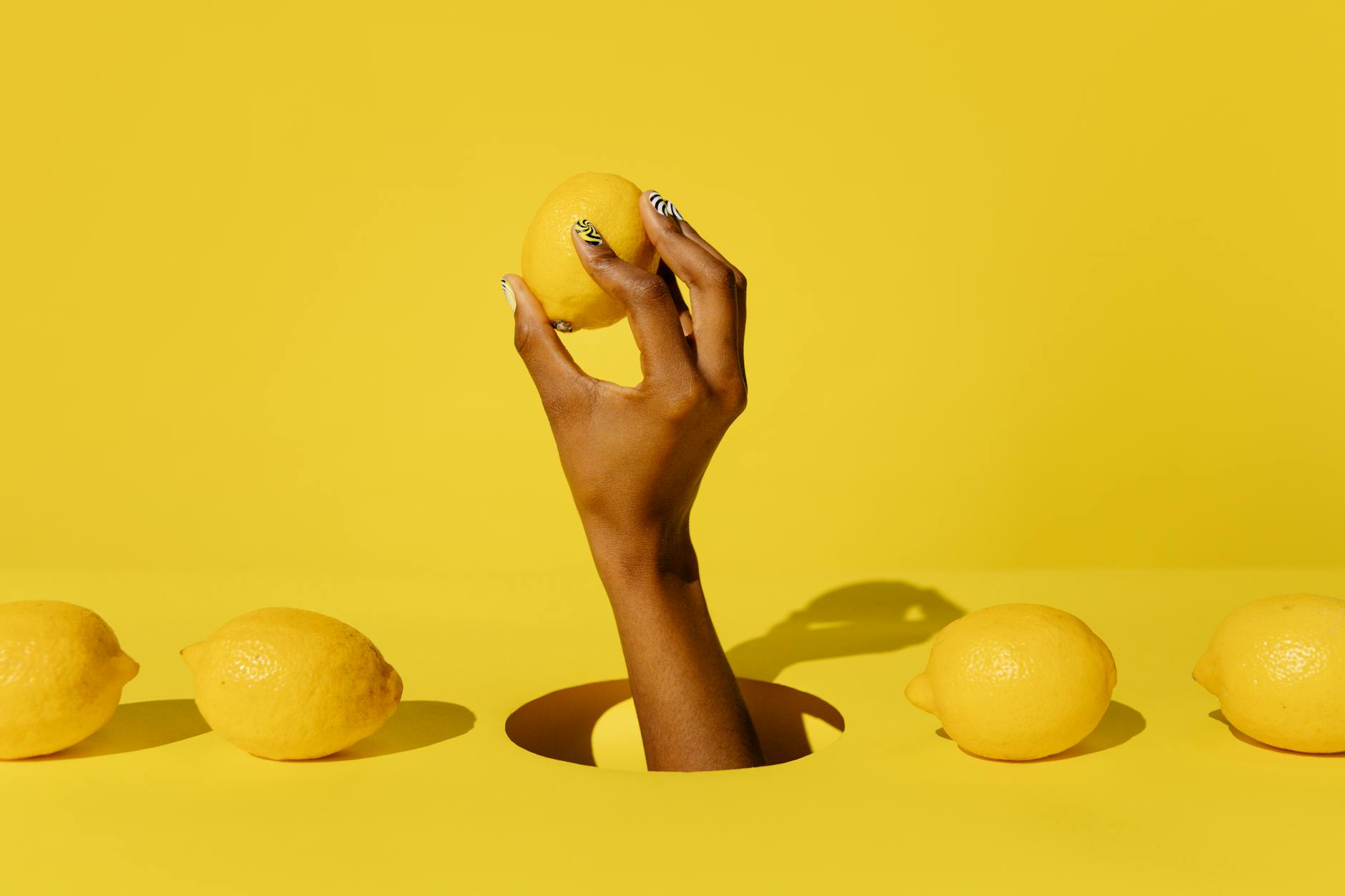 Hand holding a fresh lemon against a yellow background, symbolizing renewal and fresh starts