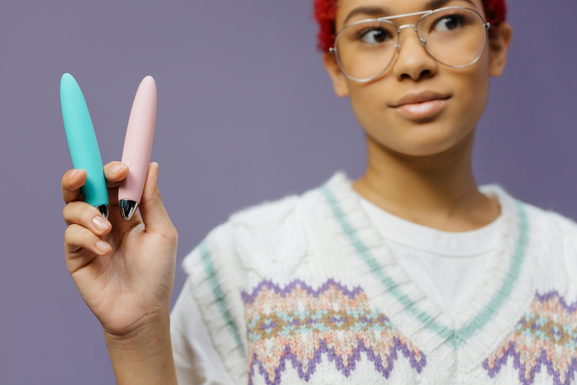 Hands gently holding a blue silicone clitoral vibrator against a soft purple background