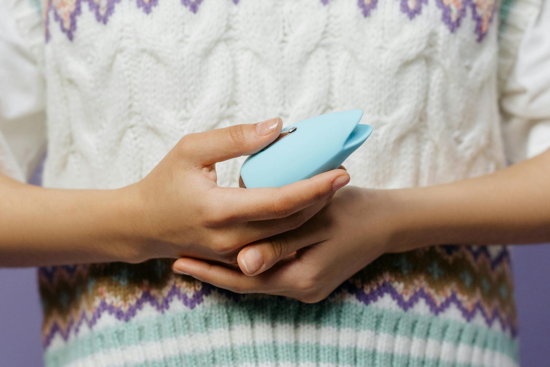 Person holding a blue personal massager against a knitted sweater, preparing for solo exploration
